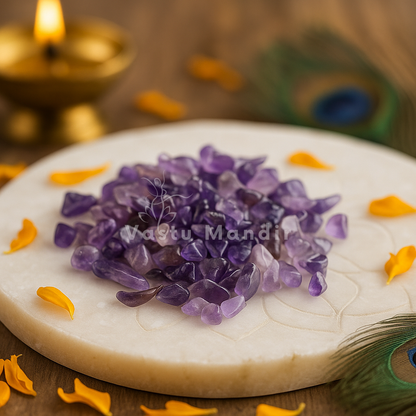 Amethyst crystal chips on a white stone with 'Vastu Mandi' branding, surrounded by yellow petals and a lit candle.