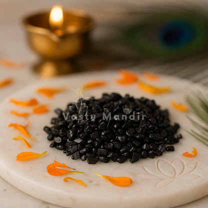 Black Tourmaline Vastu Chips on a decorative plate with orange petals and a lit lamp in the background, featuring 'Vastu Mandir' branding.