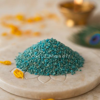 Blue Apatite Chips on a decorative stone surface with blurred peacock feather and flowers in the background.