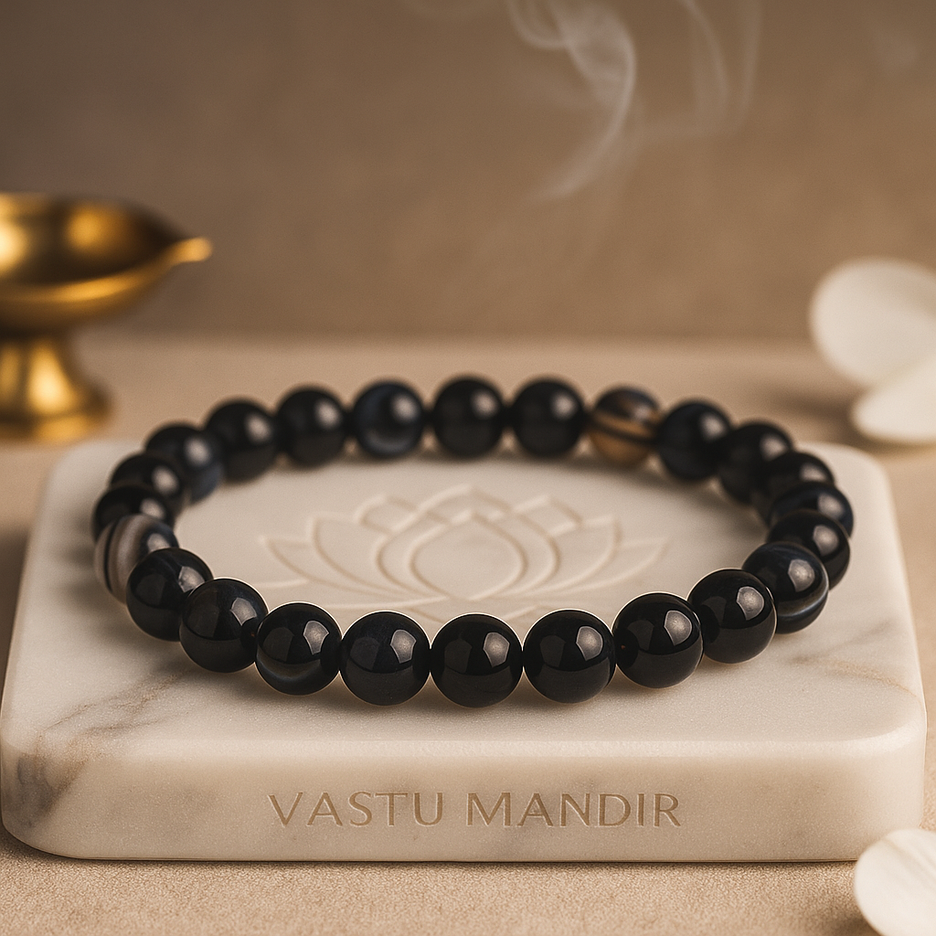 Black Agate 8mm bead bracelet on a marble tray with 'Vastu Mandir' branding, next to a gold lamp.