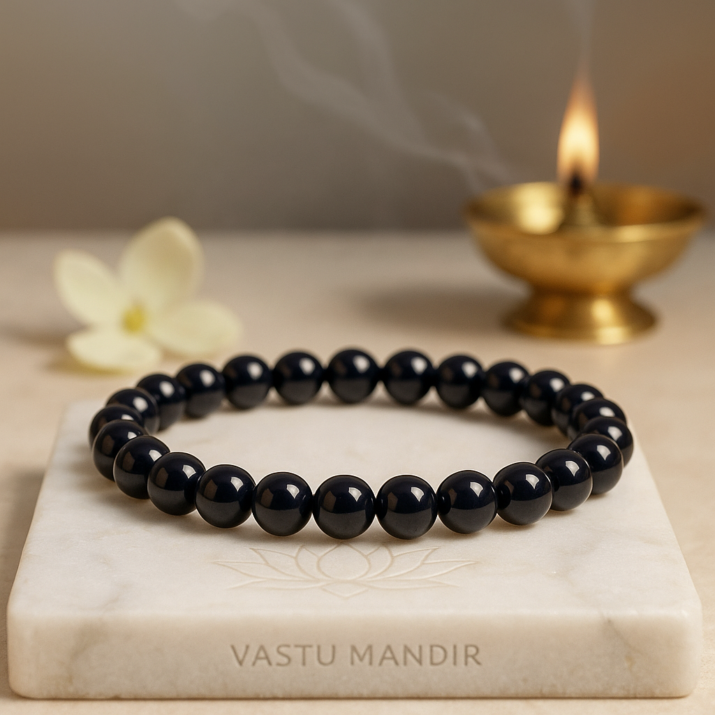Black Onyx 8mm bead bracelet on a marble slab with a lit candle in the background, branded 'Vastu Mandir'.