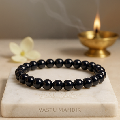Black Onyx 8mm bead bracelet on a marble slab with a lit candle in the background, branded 'Vastu Mandir'.