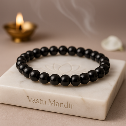 Black Onyx 8mm bead bracelet on a marble stand with 'Vastu Mandir' branding, candle, and white flower in the background.