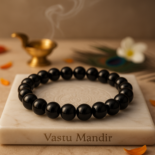 Black garnet 8mm crystal bead bracelet on a marble surface with 'Vastu Mandir' branding, accompanied by a small lamp and flowers.