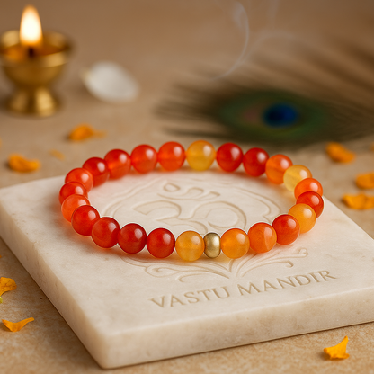 Natural red agate 8mm crystal bead bracelet on a marble slab with 'Vastu Mandir' branding, candle, and peacock feather in the background.