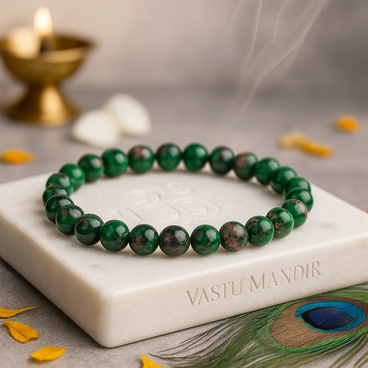 Green beaded ruby zoisite 8mm bead bracelet on a marble stand with 'Vastu Mandir' branding, candles, and peacock feather in the background.