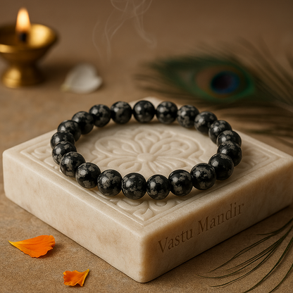 natural snowflake obsidian 8mm crystal bead bracelet on a decorative stone block with a peacock feather and candle in the background.