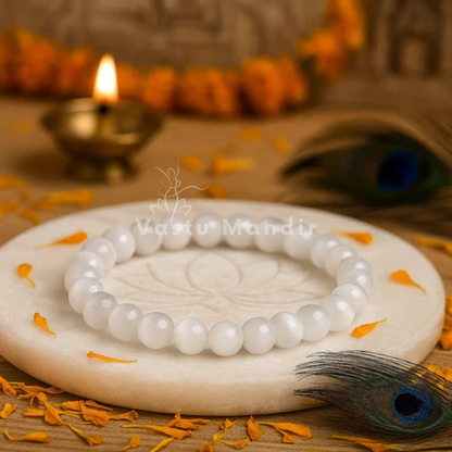 100% Natural Selenite beads with pristine white coloration and luminous transparency on a decorative stone surface with flowers and a lit lamp in the background.