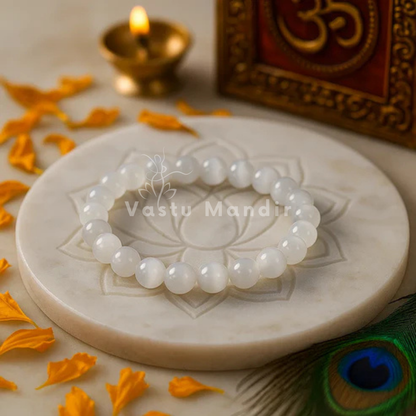 100% Natural Selenite beads with pristine white coloration and luminous transparency on a decorative stone surface with 'Vastu Mandir' branding.
