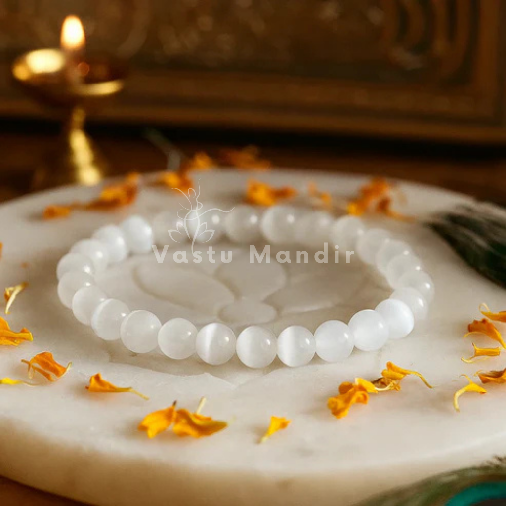 100% Natural Selenite beads with pristine white coloration and luminous transparency on a marble surface with yellow flowers and 'Vastu Mandir' branding.