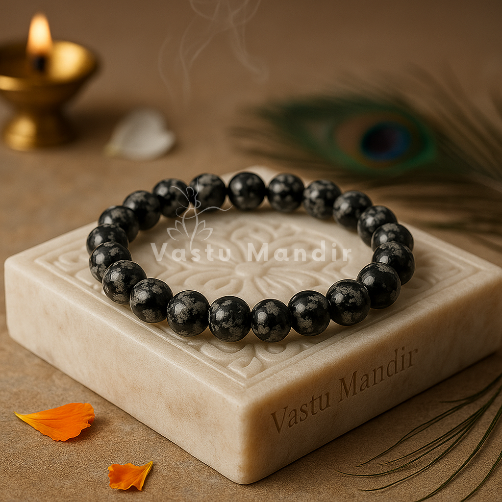 100% Natural Snowflake Obsidian beads with distinctive black base and white snowflake-like cristobalite inclusions on a stone plinth with 'Vastu Mandir' branding, surrounded by decorative elements.