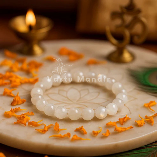 100% Natural Rainbow Moonstone (White) on a decorative plate with flowers and a candle in the background, branded 'Vastu Mandir'.