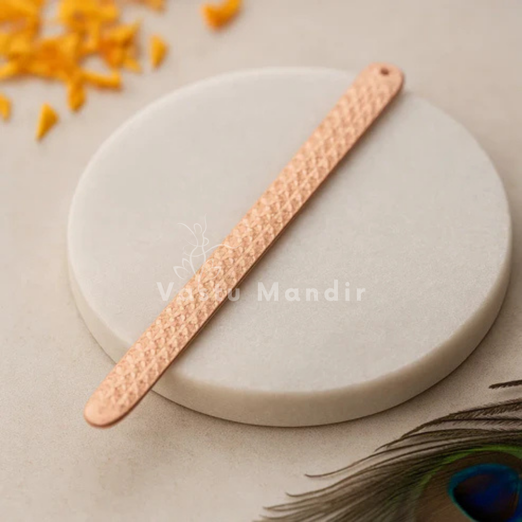 Pyramid Strip 10.5 inches for Vastu Remedy in Copper on a white stone with 'Vastu Mandir' branding, surrounded by yellow flowers and a peacock feather.