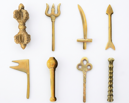 brass-colored metallic Astra Shastra Collection pieces with traditional Indian symbolic designs, arranged in two rows of four on a clean white background.