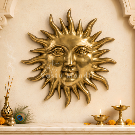 A large metallic gold sun wall sculpture with a human face and radiating rays, mounted on a beige wall above a mantel with lit oil lamps, incense, and small orange flowers.