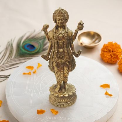 Brass Dhanvantri statue on a white platform with marigold flowers and a peacock feather.