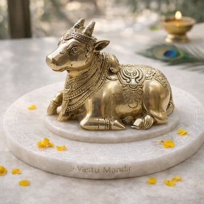 Vastu brass bull statue on a marble base with 'Vastu Mandir' branding, surrounded by yellow flowers.