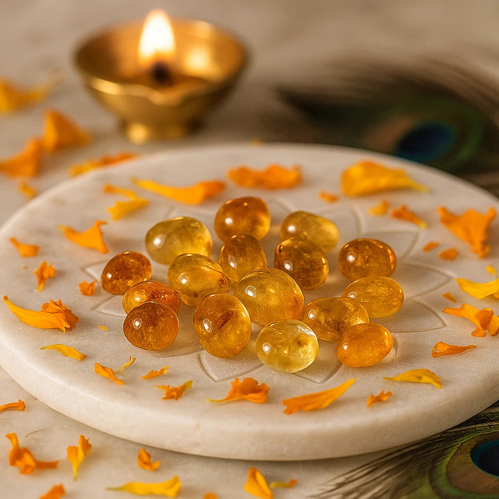 Angled view of citrine tumbled stones on a white plate with marigold petals and a peacock feather