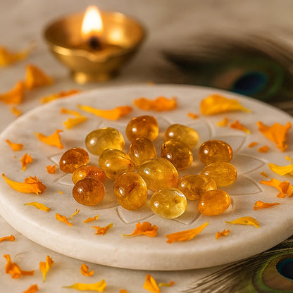 Angled view of citrine tumbled stones on a white plate with marigold petals and a peacock feather
