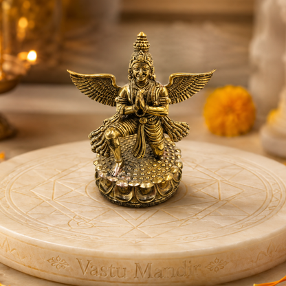 Garud Dev Brass Idol on a circular stone platform with 'Vastu Mandir' engraved, surrounded by decorative elements.