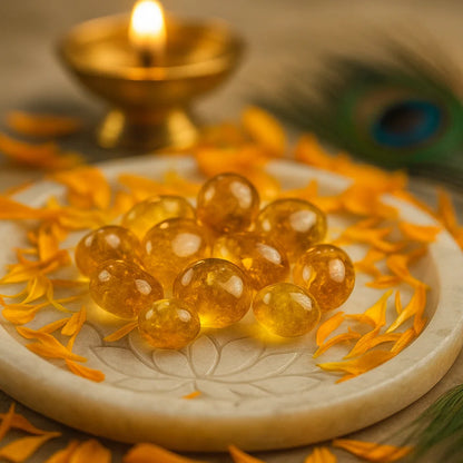 Citrine tumbled stones arranged on a carved white plate with marigold petals and a softly lit diya
