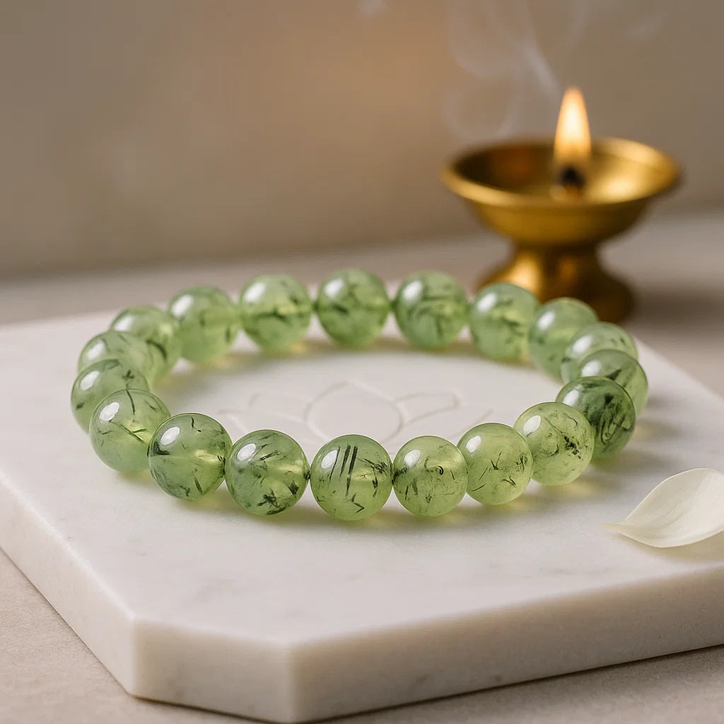 Green beaded bracelet on a marble surface with a lit candle in the background