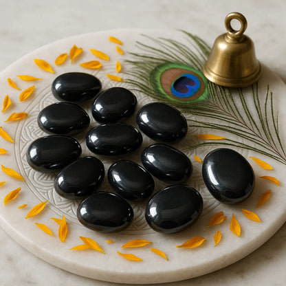 Polished hematite crystals for focus and healing energy on a decorative plate with peacock feather and brass bell