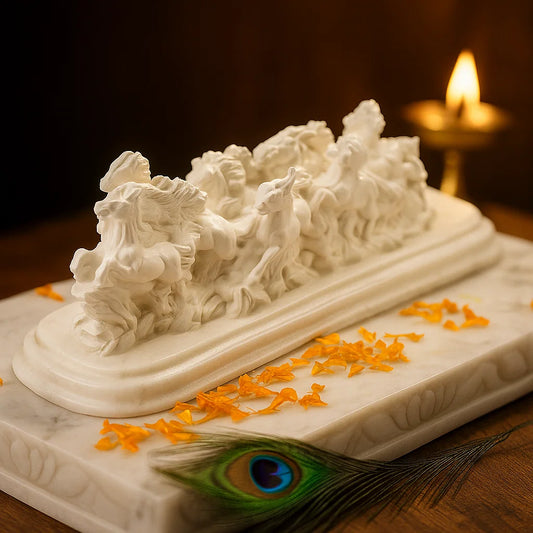 White marble sculpture of a two horses on a white marble surface with orange blossoms and a peacock feather on a wooden surface.
