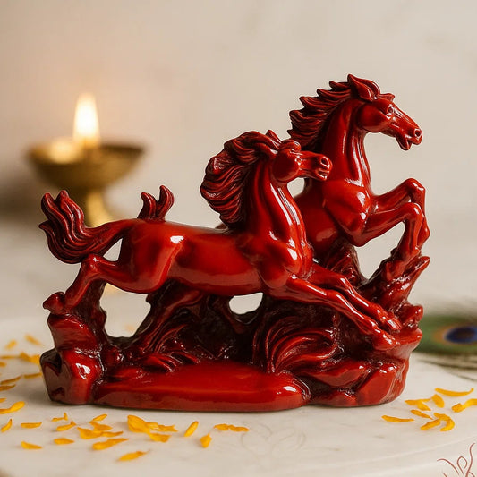 Red ceramic sculpture of two horses on a marble surface with a candle in the background