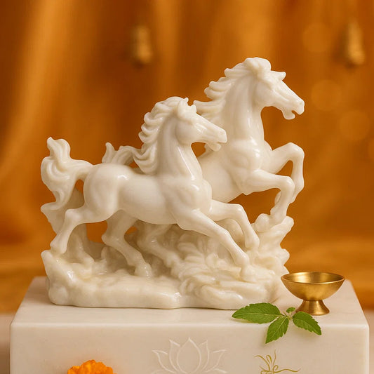 White marble sculpture of two horses on a white base against an orange fabric background.