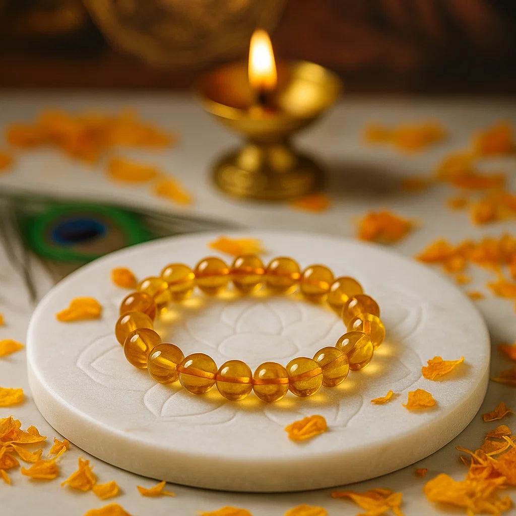 Citrine 10mm bead bracelet on a white stone surface with orange flower petals and a lit oil lamp in the background.