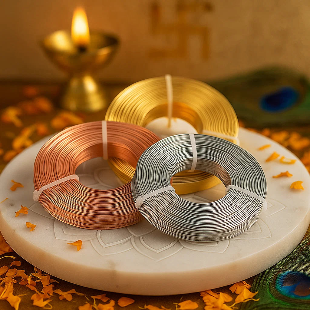 Three spools of wire in brass, silver, and copper on a decorative plate with a candle in the background.