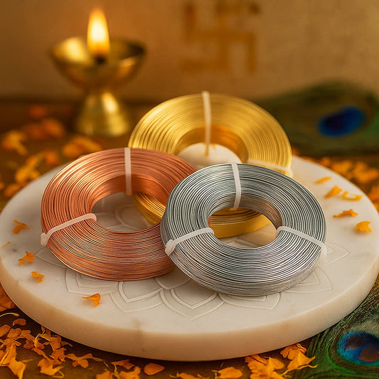 Three spools of wire in brass, silver, and copper on a decorative plate with a candle in the background.