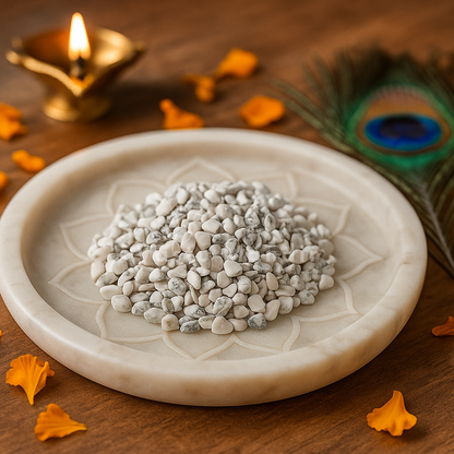 Howlite Chips with pebbles, peacock feather, and lit oil lamp on a wooden surface.